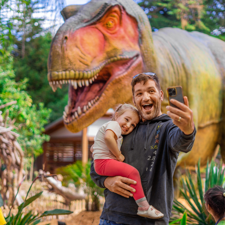 Parent and child taking a selfie in front of animatronic T Rex